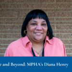 A person wearing a coral shirt and gold earrings stands against a brick wall, smiling. Text overlay reads: "Going Above and Beyond: MPHA’s Diana Henry."