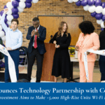 A group of people participates in a ribbon-cutting ceremony indoors, with a purple and white balloon arch in the background.
