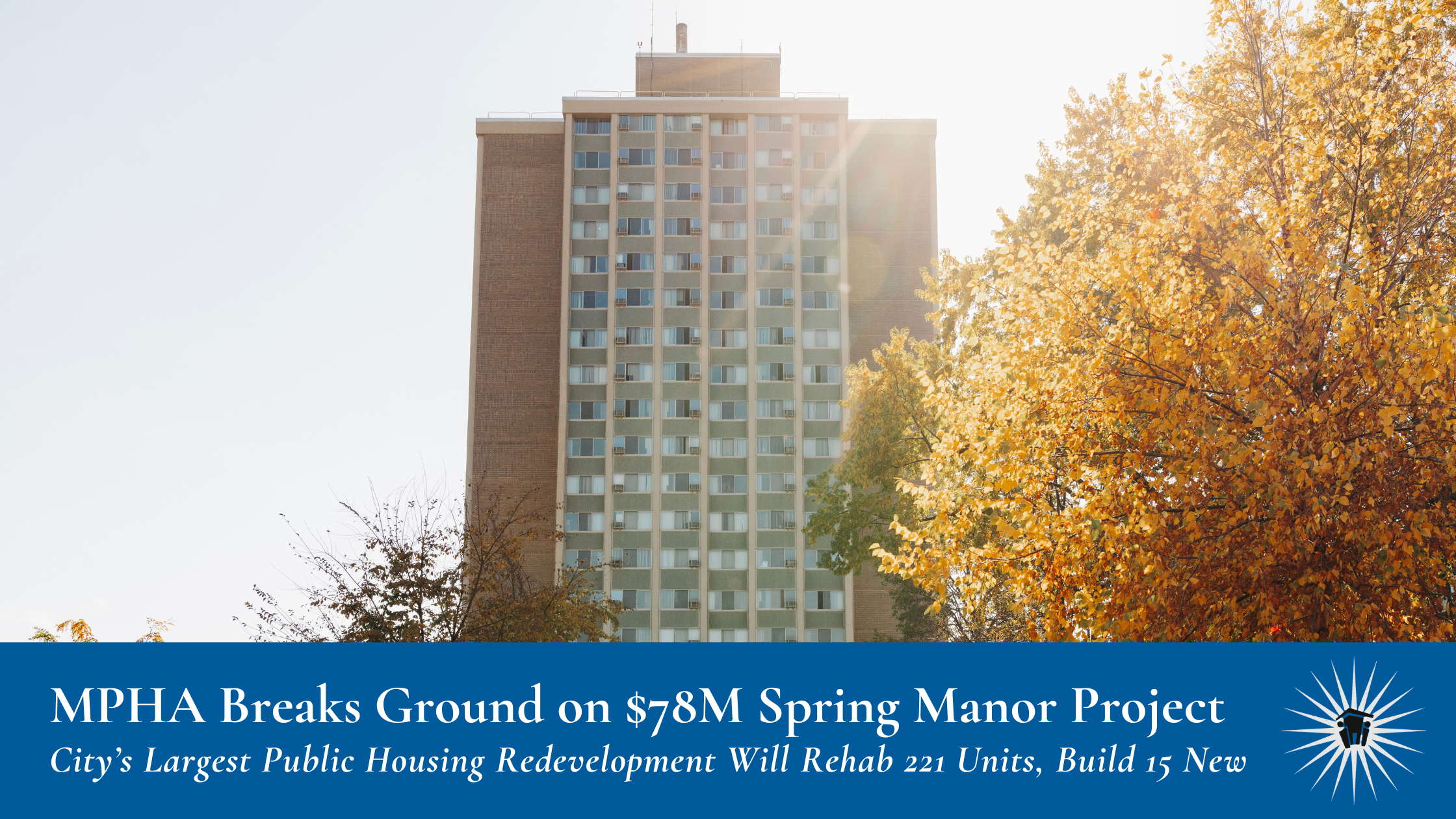 A tall apartment building with many windows stands behind autumn trees with yellow and orange leaves on a sunny day.