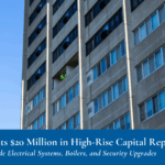 Worker installs windows on tall, gray apartment building in front of a clear blue sky.