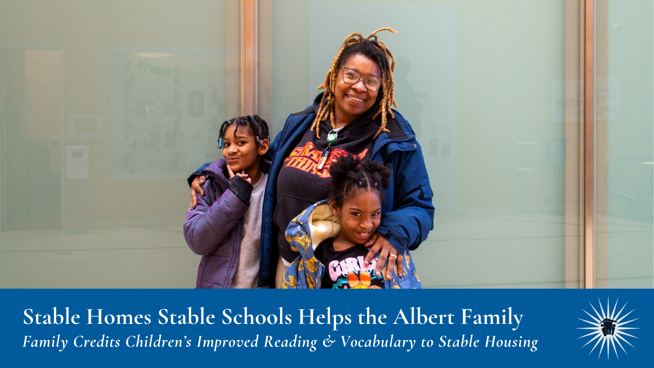 A woman stands smiling with two young girls in front of a light-colored wall. Text below reads "Stable Homes Stable Schools Helps the Albert Family, Family Credits Children’s Improved Reading & Vocabulary to Stable Housing"
