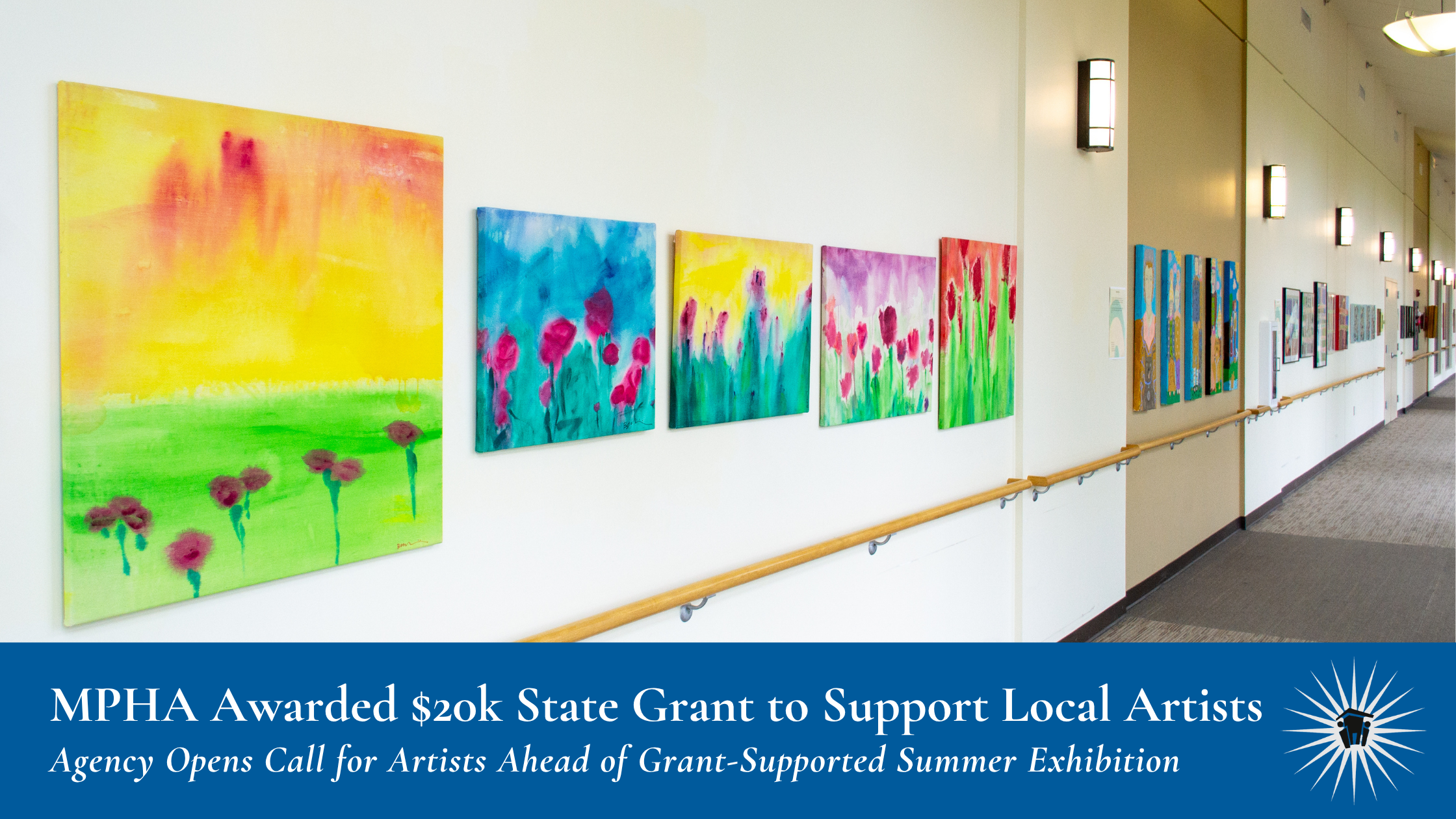 A hallway with colorful floral paintings displayed on a white wall, lit by wall-mounted lights, with a handrail and carpeted floor.